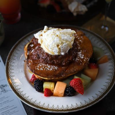 Pancakes with mixed fruit, topped with whipped cream, jam, and powdered sugar.