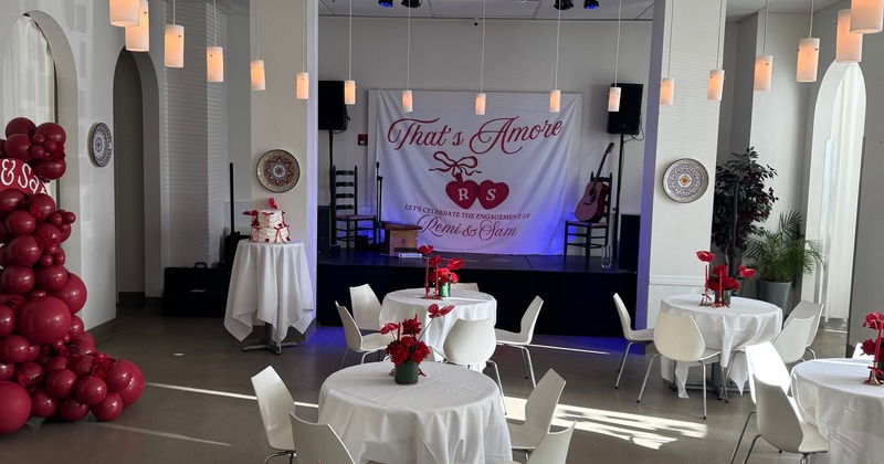 Elegant engagement party setup with white draped tables, red floral centerpieces, and a balloon arch
