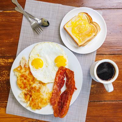 Sunny-side-up eggs with crispy bacon, hash browns, buttered toast, and coffee.