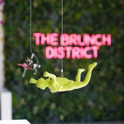 A hanging decoration with the Brunch District pink neon sign on a green wall.