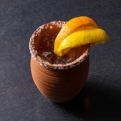 Palomoso cocktail served in salt rimmed clay pot, garnished with citrus wedges.