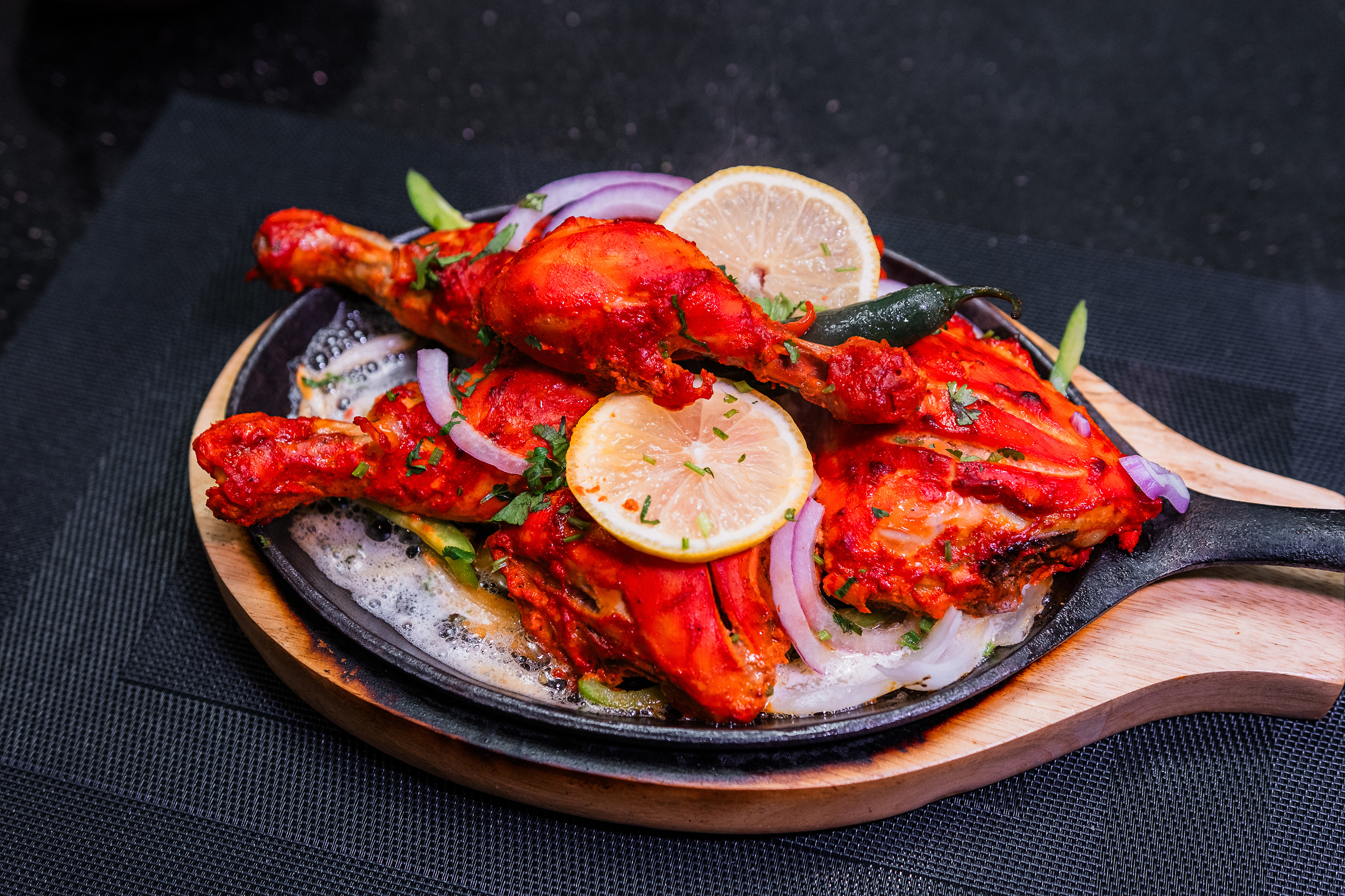 Tandoori chicken served in a skillet with lemon slices and onions