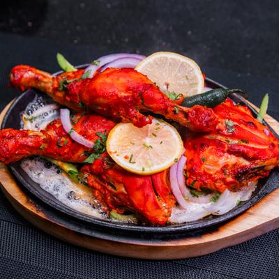 Tandoori chicken served in a skillet with lemon slices and onions.