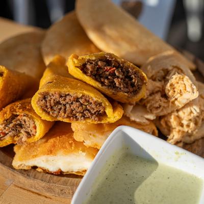 A plate of empanadas - meat and chicken fillings, with a side of green sauce.