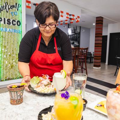 Wait staff member serving ceviche at a restaurant table.