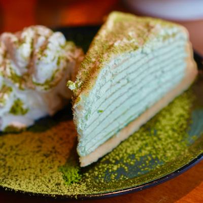 Matcha crepe cake slice served with whipped cream and green tea powder.