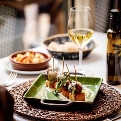 Three skewered gourmet bites drizzled with sauce, garnished with rosemary, served with white wine.