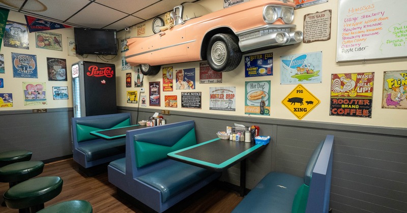 Retro-themed diner with vintage signs and a mounted pink classic car on the wall.