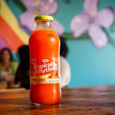 A bottle of mango carrot juice with a colorful mural in the background.