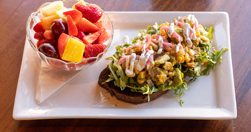 Bread  topped with avocado, corn, arugula and cream, a cup of fruit