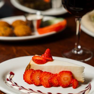 Cheesecake topped with sliced strawberries, beside a glass of wine.