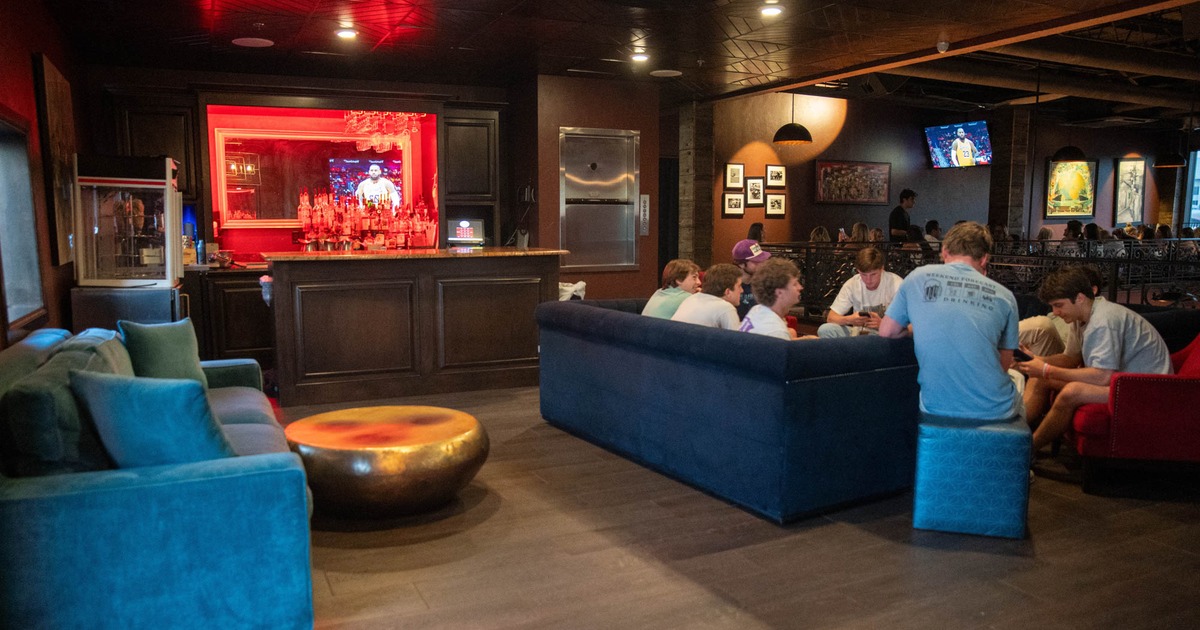 Lounge area with a bar, sofas, guests, and TVs