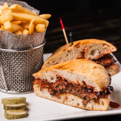 BBQ brisket sandwich served with fries and pickle slices.