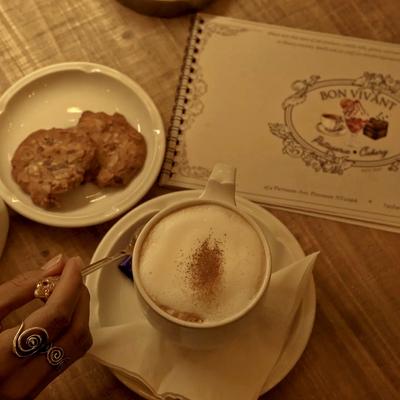 Foamy cappuccino on saucer with cookies and spoon.