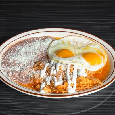 Chilaquiles served with sunny-side eggs and refried beans on a plate.