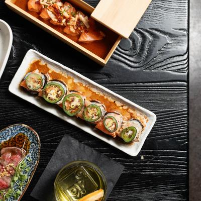 Sushi rolls and sashimi with a drink on a black table.