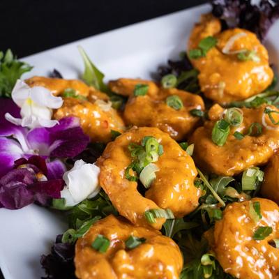 Fried shrimp in a creamy Sriracha sauce with green onion, garnished with flowers.