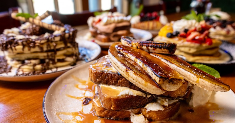Thick-cut French toast topped with caramelized bananas, served alongside decadent pancakes