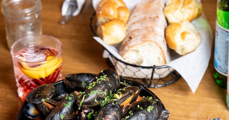 A table with served mussels, a cocktail, bread and a soup