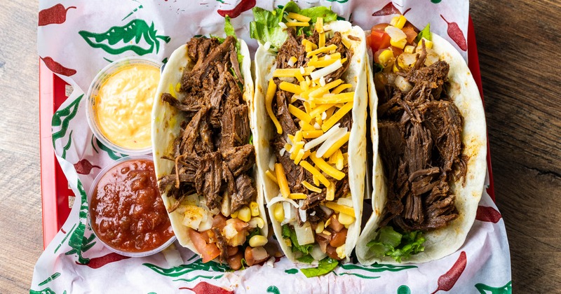 Three soft-shell tacos filled with shredded beef and various toppings