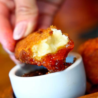 Fried cheese stick being dipped into a cup of jam.