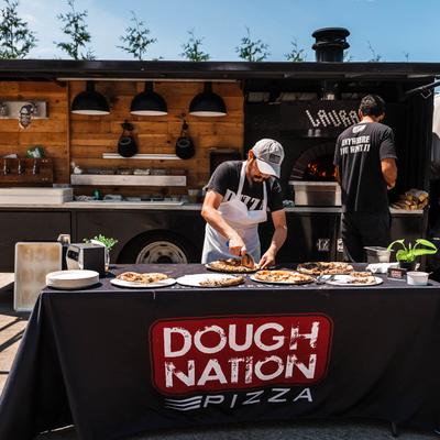 A pizza truck with one person cutting pizzas.