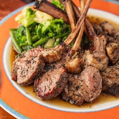 A white plate holds sliced lamb chops, broccoli, and mashed potatoes.