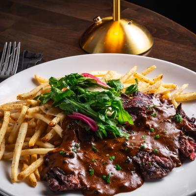 Steak topped with gravy and served with fries and greens.