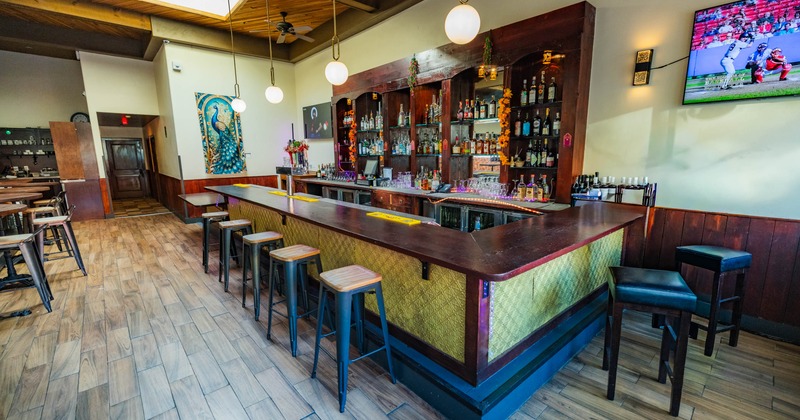 Interior of a bar with a U-shaped counter, high stools, shelves with bottles
