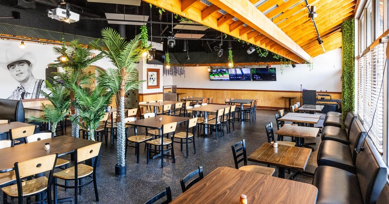 Interior,  wooden tables, chairs, palm plants, a mural with portraits, decorative lighting