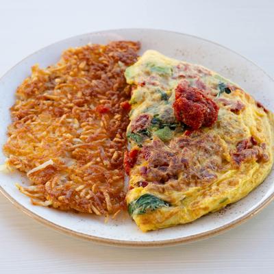 California omelet topped with sun-dried tomatoes, accompanied by crispy hash browns.