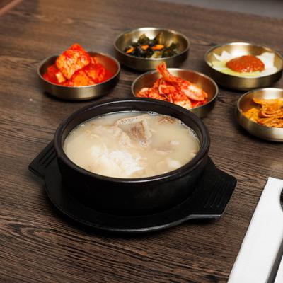 Bowl of Korean ox tail soup served alongside small metal bowls of banchan.