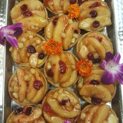 Assorted fruit tarts topped with glazed apple slices and cranberries on a metal tray.