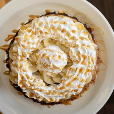 Overhead view of an oatmeal waffle topped with banana slices, whipped cream, and caramel drizzle.