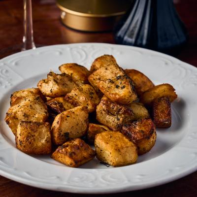 Golden roasted potatoes on a round white plate.