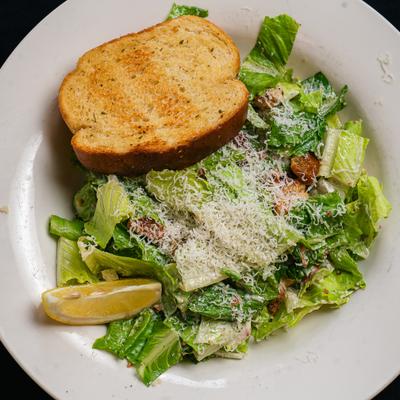Caesar salad served with toasted bread and a lemon wedge.