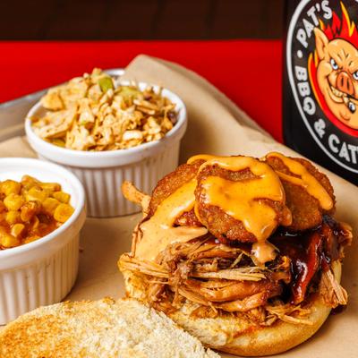 Fried Pickle and pork Sammy with sides of coleslaw, Cajun corn, and bread.