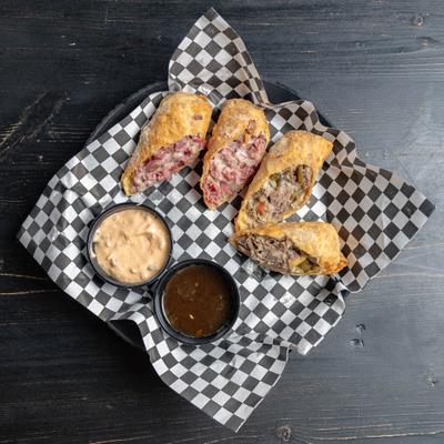 Egg rolls cut in half, served on a checkered paper liner with two dipping sauces.