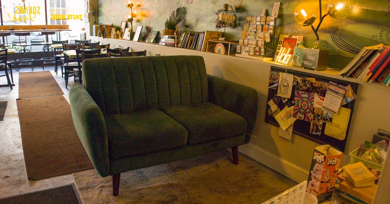 Cozy interior with a green couch, bulletin board covered in artwork, and wooden tables and chairs