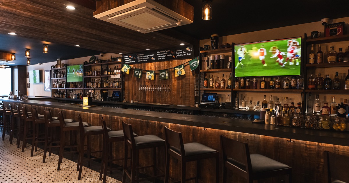 A long bar with lined-up upholstered stools and TVs