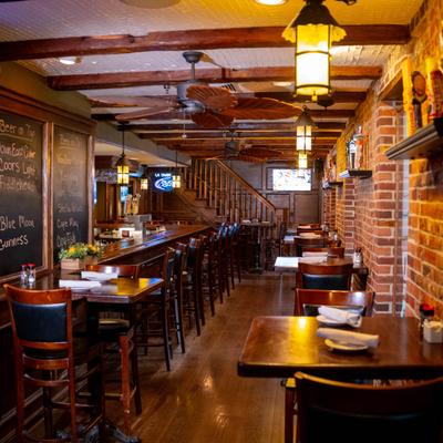 Interior with a long bar on the left, lined with high chairs, dining tables are on the right.