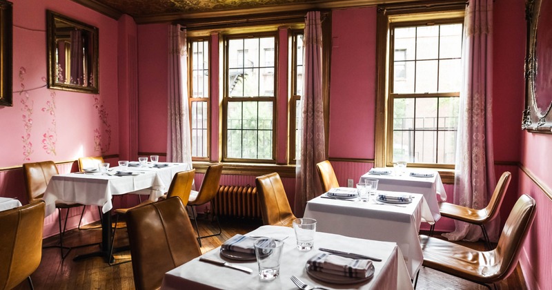 A pink-walled dining room with gold mirrors and leather chairs