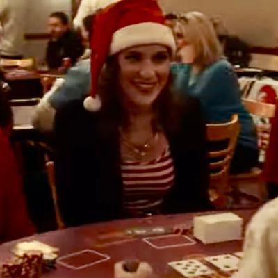 A person in a Santa hat smiling at a card table in a busy room.
