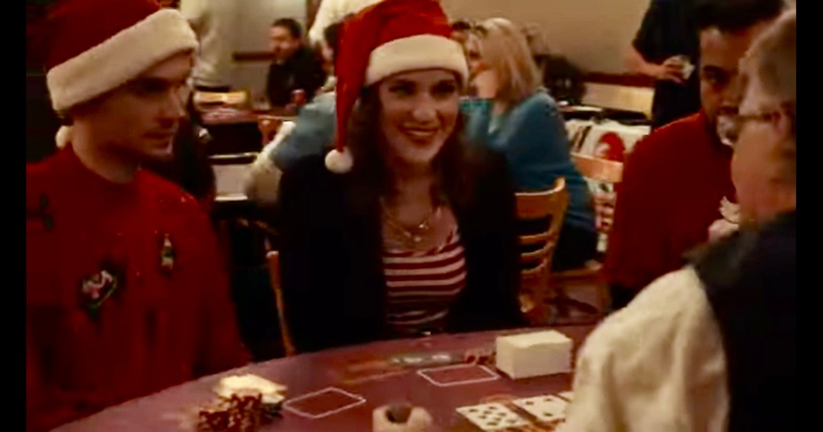 A person in a Santa hat smiling at a card table in a busy room