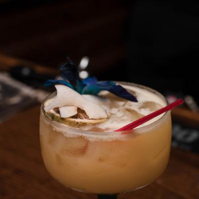 Cocktail in a steamed glass garnished with coconut flakes and a flower.