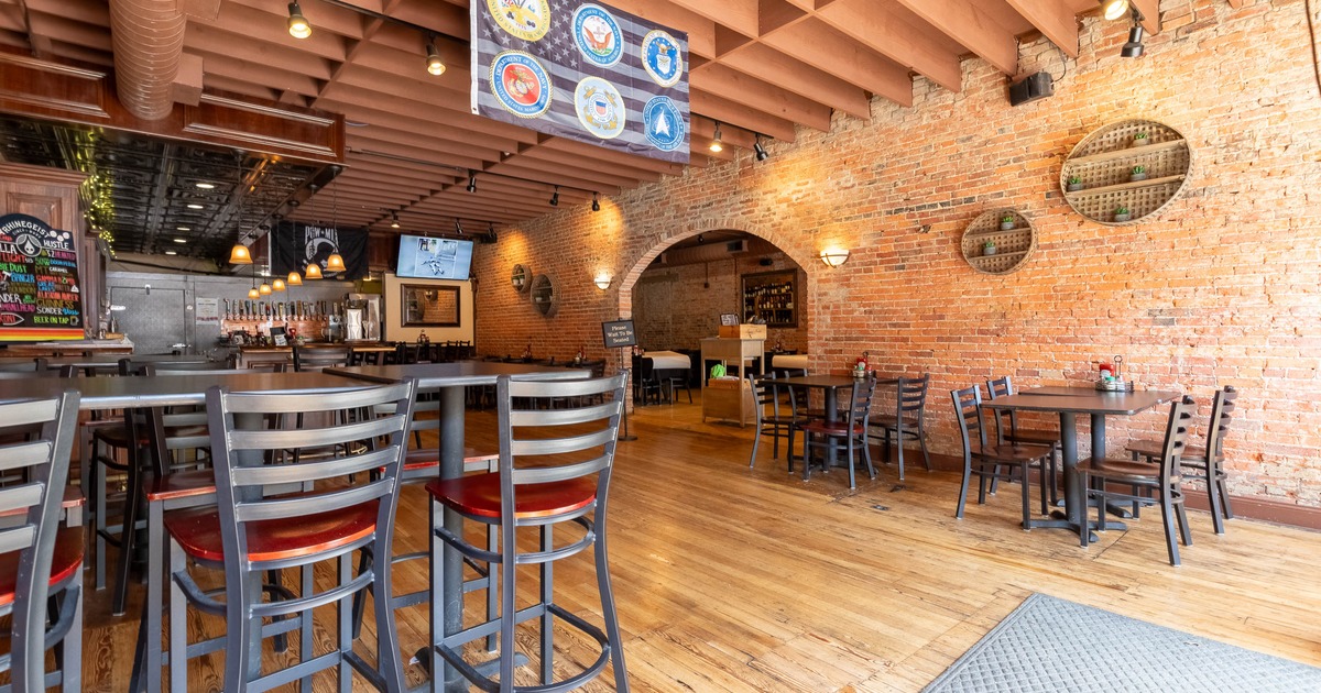 Interior of a rustic restaurant with wooden floors, exposed brick walls, and a bar area