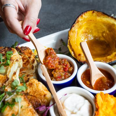 hand reaches for condiments on a fall-colored assortment of vegetable dishes
