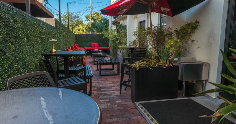 Outdoor seating area, brick pathway, black tables, red cushioned chairs, plants