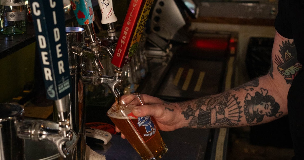 A bartender is pouring a draft beverage, likely a beer or cider, into a glass at a bar