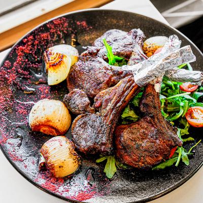 A platter with Lamb chops, grilled onions, and arugula salad with cherry tomatoes.